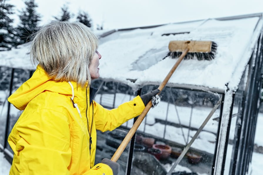 Žena odklízející sníh ze skleníku pomocí smetáku